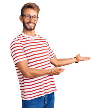 Handsome blond man with beard wearing casual clothes and glasses inviting to enter smiling natural with open hand
