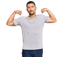 Handsome man with tattoos wearing 90s style showing arms muscles smiling proud. fitness concept.