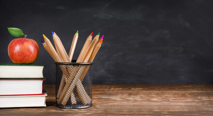 Stack of books with apple on the top and pencils in the pot on the table against blackboard background, copy space. Back to school concept