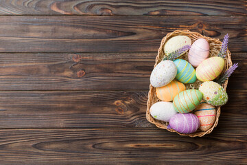 Colorful Easter eggs in wicker basket against colored background, closeup. top view with copy space