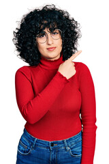 Young middle east girl wearing casual clothes and glasses pointing with hand finger to the side showing advertisement, serious and calm face