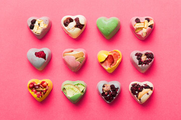 Fototapeta premium chocolate sweets in the form of a heart with fruits and nuts on a colored background. top view with space for text, holiday concept