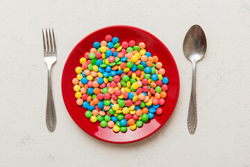 cutlery on table and sweet plate of candy. Health and obesity concept, top view on colored background