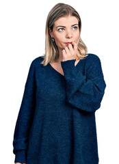 Young blonde woman wearing casual sweater looking stressed and nervous with hands on mouth biting nails. anxiety problem.