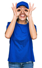 Young hispanic girl wearing delivery courier uniform doing ok gesture like binoculars sticking tongue out, eyes looking through fingers. crazy expression.
