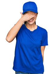 Young hispanic girl wearing delivery courier uniform smiling and laughing with hand on face covering eyes for surprise. blind concept.