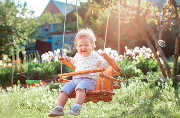 Happy International Children's Day. Smiling toddler girl having fun on a swing. Sunny summer...