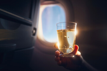 Man enjoying drink during flight. Passenger holding glass of sparkling wine against airplane...
