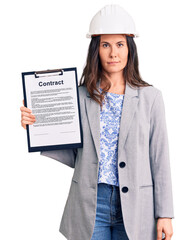 Young beautiful brunette woman wearing architect hardhat holding contract thinking attitude and sober expression looking self confident