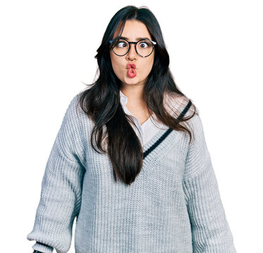 Beautiful hispanic woman wearing casual sweater and glasses making fish face with lips, crazy and comical gesture. funny expression.