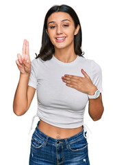 Young hispanic girl wearing casual white t shirt smiling swearing with hand on chest and fingers...
