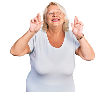 Middle age blonde woman wearing casual white t shirt gesturing finger crossed smiling with hope and eyes closed. luck and superstitious concept.