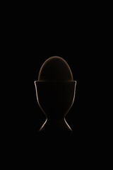 Dark Easter egg in a cup on black background with silhouette rim light  and flare