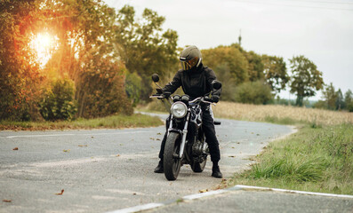 motorcyclist in motorcycle clothing and a helmet on an old motorcycle cafe racer in the summer on...