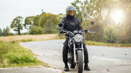 motorcyclist in motorcycle clothing and a helmet on an old motorcycle cafe racer in the summer on the road