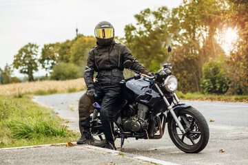 motorcyclist in motorcycle clothing and a helmet on an old motorcycle cafe racer in the summer on the road