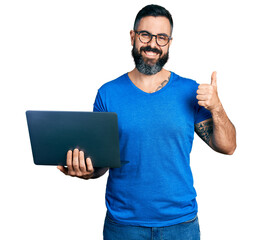 Hispanic man with beard working using computer laptop smiling happy and positive, thumb up doing...