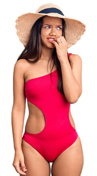 Young beautiful latin girl wearing swimwear and summer hat looking stressed and nervous with hands on mouth biting nails. anxiety problem.