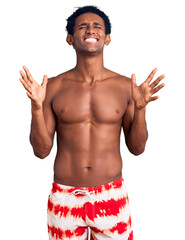 Fototapeta premium African handsome man wearing swimsuit and sunglasses celebrating mad and crazy for success with arms raised and closed eyes screaming excited. winner concept