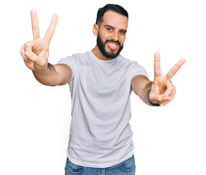 Young man with beard wearing casual white t shirt smiling with tongue out showing fingers of both hands doing victory sign. number two.