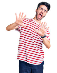 Naklejka premium Young hispanic man wearing casual clothes afraid and terrified with fear expression stop gesture with hands, shouting in shock. panic concept.
