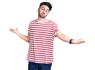 Young hispanic man wearing casual clothes clueless and confused expression with arms and hands...