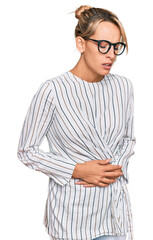 Beautiful blonde woman wearing business shirt and glasses with hand on stomach because indigestion, painful illness feeling unwell. ache concept.