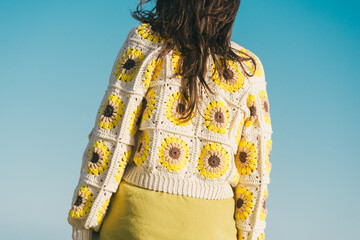 woman from behind with crochet cardigan, granny square sunflower, blue sky background - obrazy, fototapety, plakaty