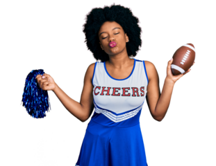 Young african american woman wearing cheerleader uniform holding pompom and football ball looking at the camera blowing a kiss being lovely and sexy. love expression.