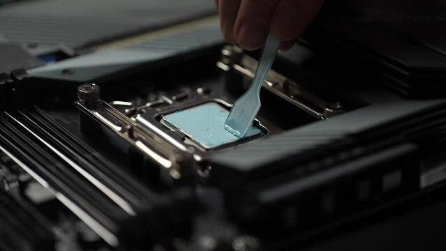 Close-up cropped shot of unrecognizable professional computer master spreading new thermal paste to computer processor before installing PC CPU air cooling system radiator. Shooting in slow motion.