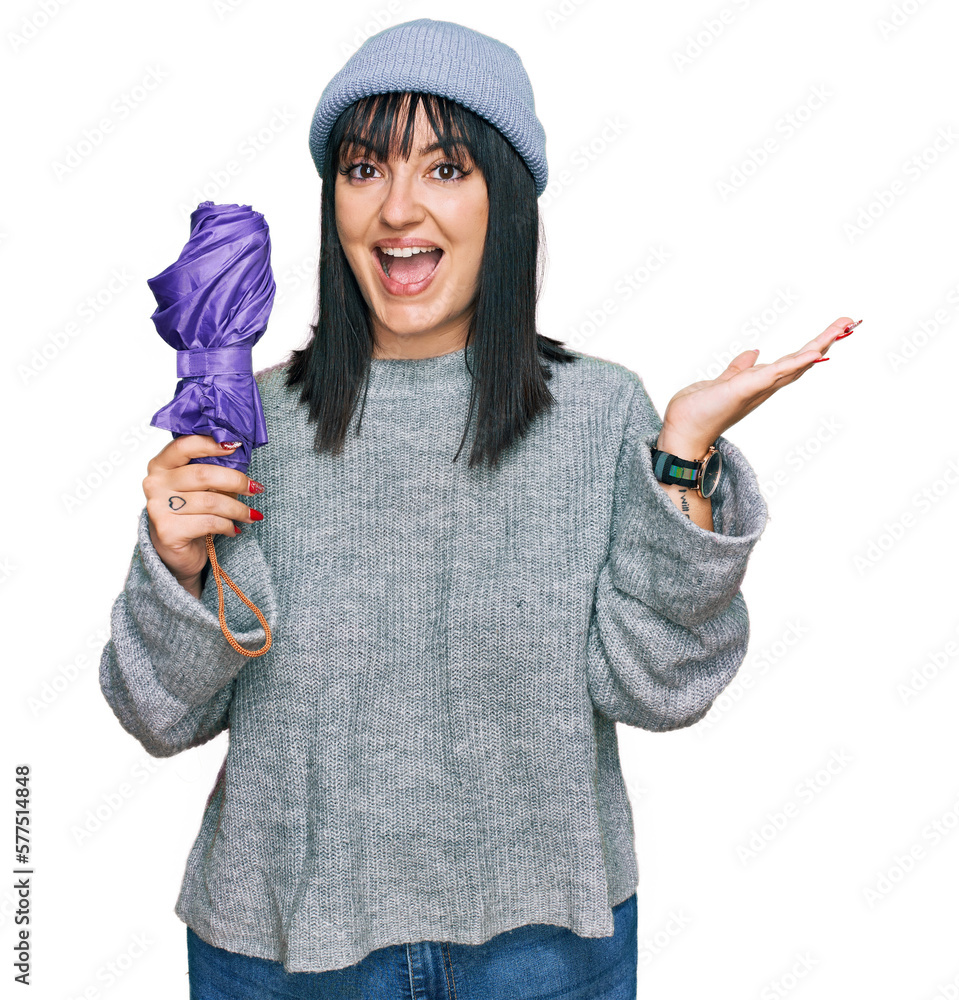 Sticker Young hispanic woman holding closed purple umbrella celebrating victory with happy smile and winner expression with raised hands