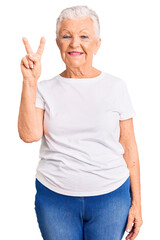 Senior beautiful woman with blue eyes and grey hair wearing casual white tshirt showing and pointing up with fingers number two while smiling confident and happy.