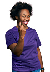 Fototapeta na wymiar African american woman with afro hair wearing casual purple t shirt beckoning come here gesture with hand inviting welcoming happy and smiling