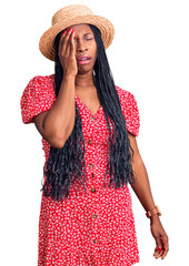 Young african american woman wearing summer hat yawning tired covering half face, eye and mouth with hand. face hurts in pain.