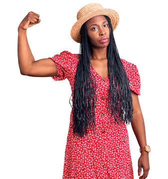 Young african american woman wearing summer hat strong person showing arm muscle, confident and proud of power