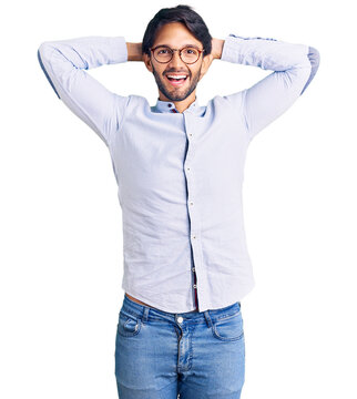 Handsome hispanic man wearing business shirt and glasses relaxing and stretching, arms and hands behind head and neck smiling happy