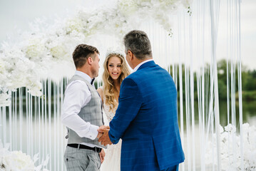 Dad congratulates the brides with a marriage and hugs. man welcomes. Happy bride and groom. On background of arch on nature in courtyard of house. Wedding ceremony. Close up.