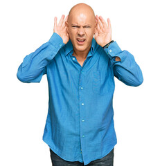 Middle age bald man wearing casual clothes trying to hear both hands on ear gesture, curious for gossip. hearing problem, deaf