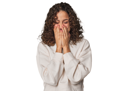 Radiant young woman with stunning curls laughing about something, covering mouth with hands.