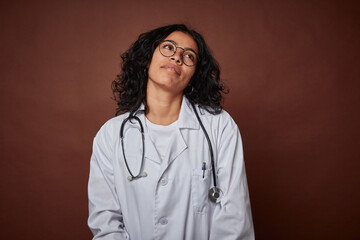 Young colombian doctor woman with stethoscope dreaming of achieving goals and purposes