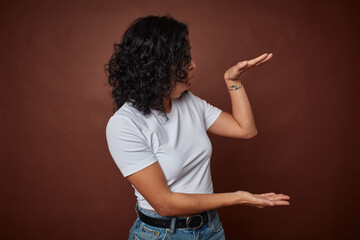 Young colombian curly hair woman isolated on brown background shocked and amazed holding a copy...