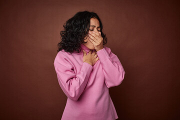 Young colombian curly hair woman isolated on brown background suffers pain in throat due a virus or...
