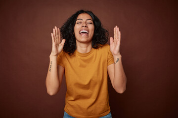 Young colombian curly hair woman isolated on brown background laughs out loudly keeping hand on chest.