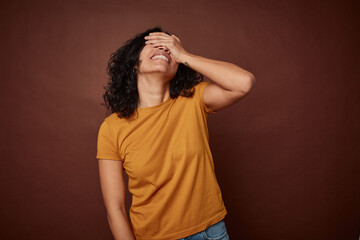 Young colombian curly hair woman isolated on brown background laughs joyfully keeping hands on head. Happiness concept.