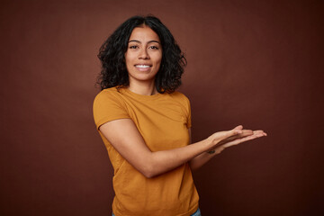 Young colombian curly hair woman isolated on brown background holding a copy space on a palm.