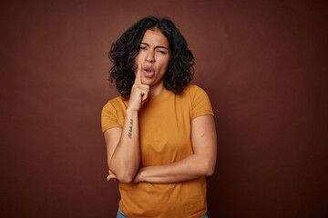 Young colombian curly hair woman isolated on brown background looking sideways with doubtful and...