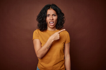 Young colombian curly hair woman isolated on brown background pointing to the side