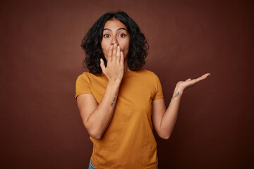 Young colombian curly hair woman isolated on brown background impressed holding copy space on palm.