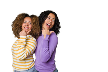 Two female friends isolated in studio points with thumb finger away, laughing and carefree.