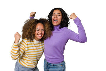 Two female friends isolated in studio raising fist after a victory, winner concept.